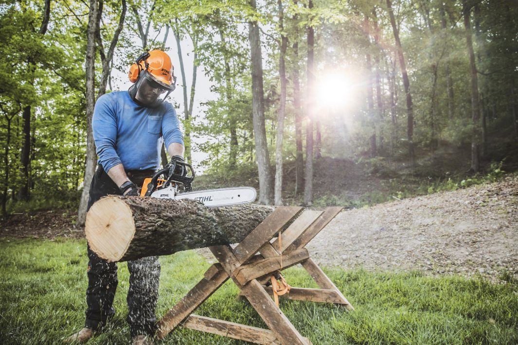 Man wearing a helmet, face shield and hearing protection cutting a log with a STIHL gas chainsaw