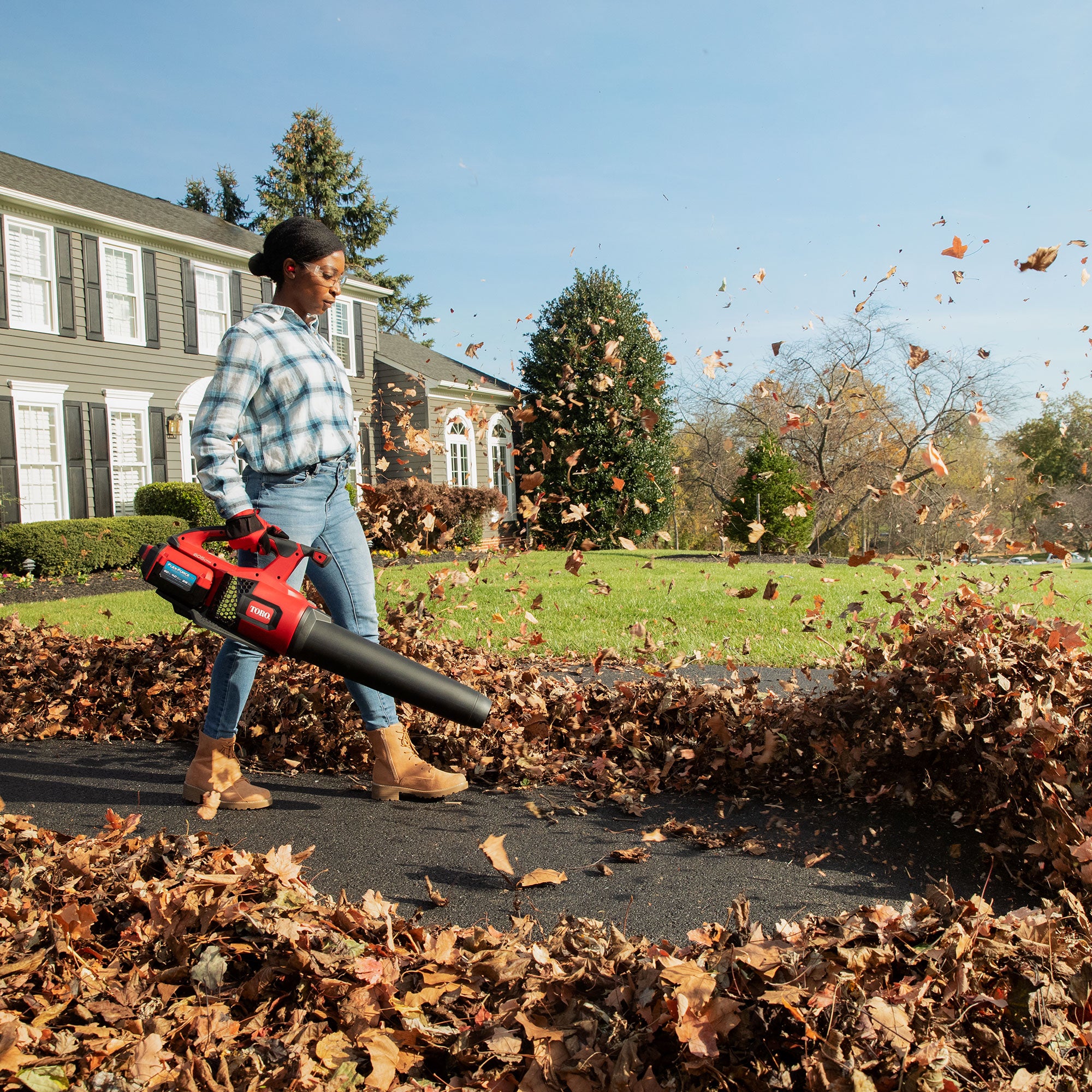 Woman clearing fall leaves from a driveway with a Toro cordless leaf blower