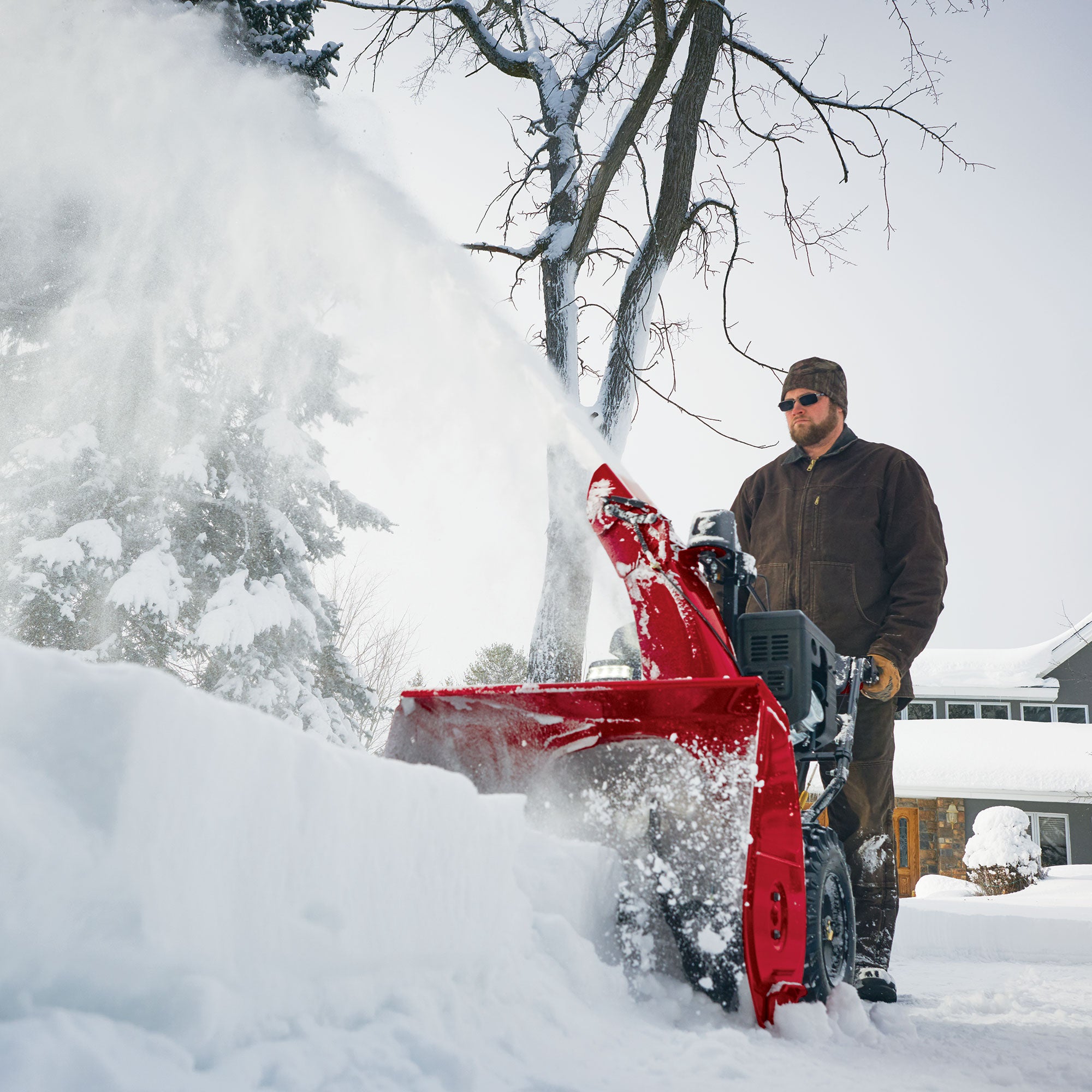 Homeowner clearing deep snow with a Toro two-stage gas snow blower in front of a house