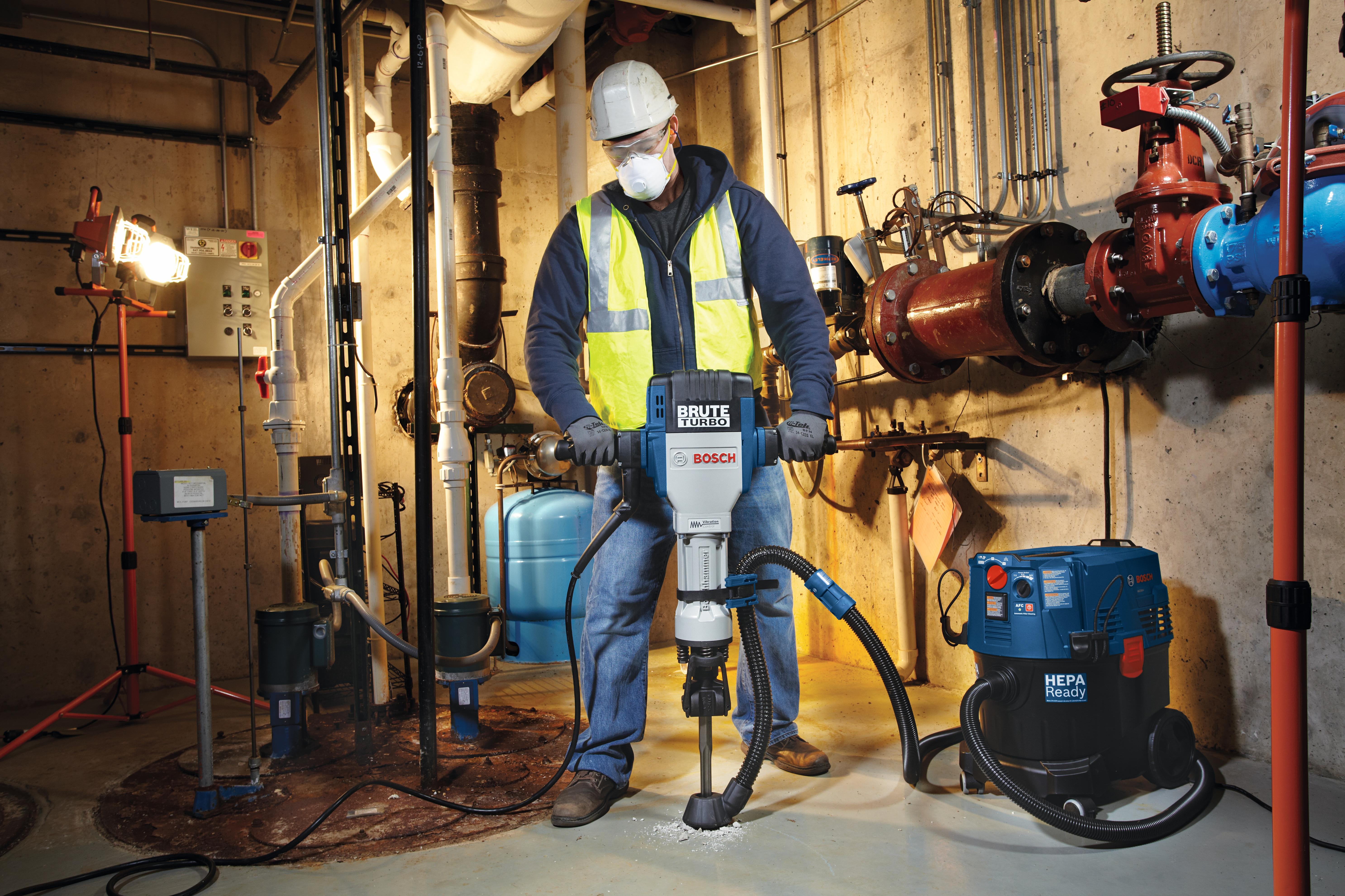 Worker breaking a basement floor with the Bosch Brute Turbo breaker and a dust extractor