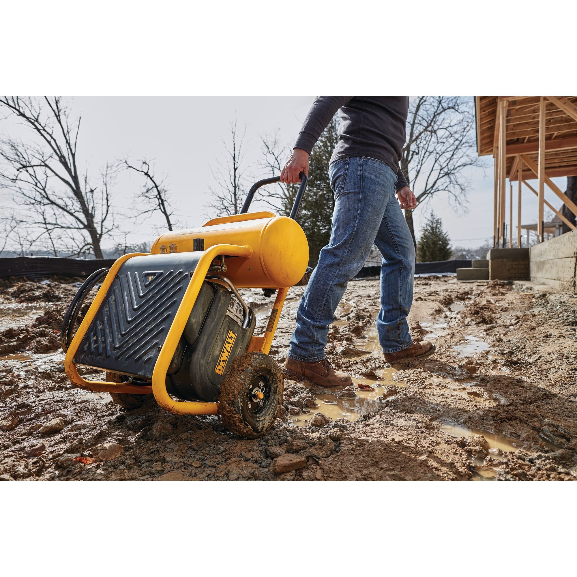 Worker wheeling the DeWalt 4.5 gallon compressor across muddy ground on a building site