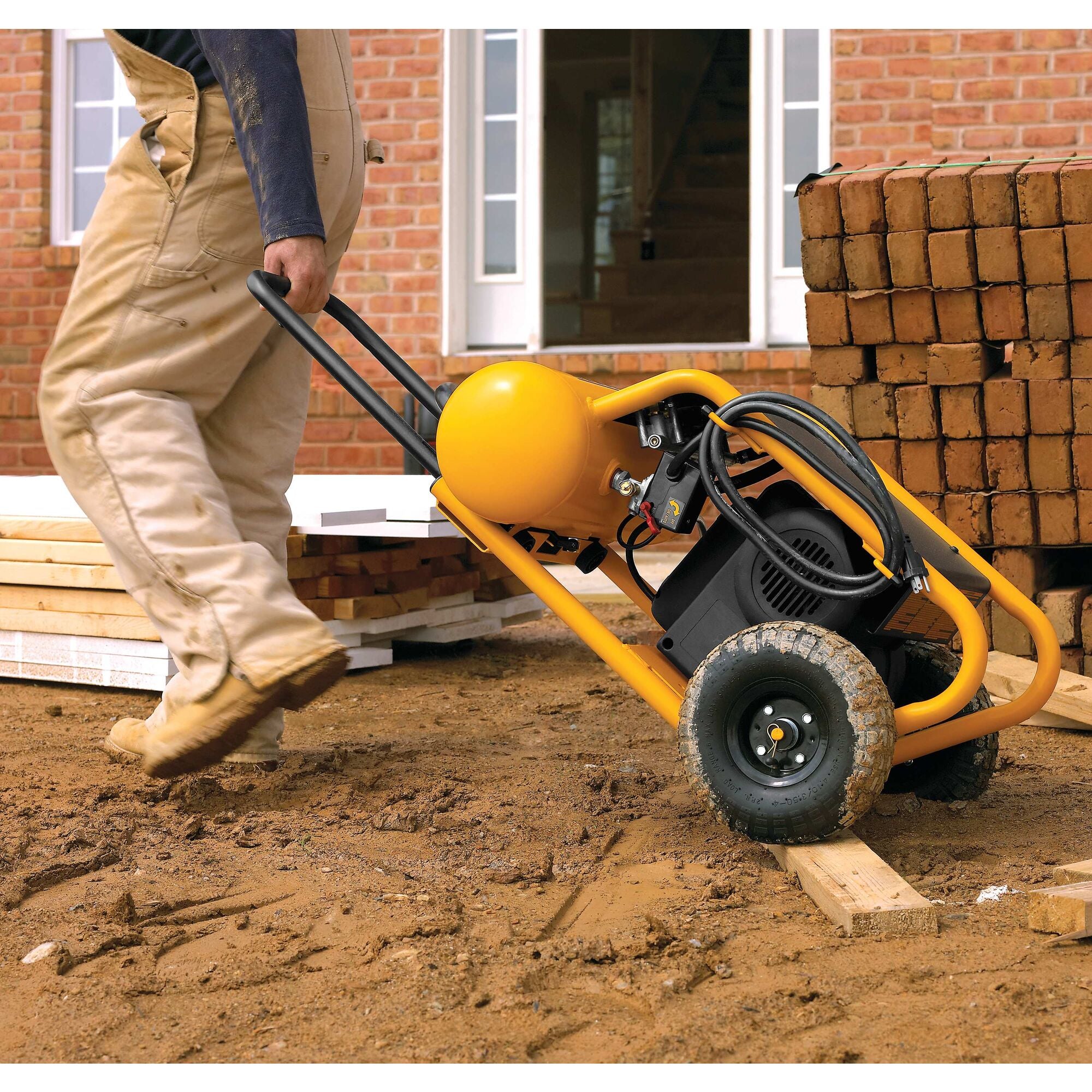 Worker pulling the DeWalt compressor over a plank on a brick-laying site