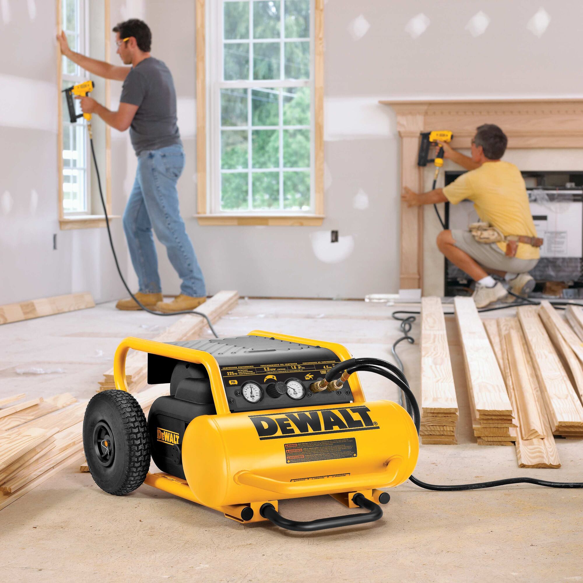 Two workers nailing trim in a room with the DeWalt 4.5 gallon compressor on the floor