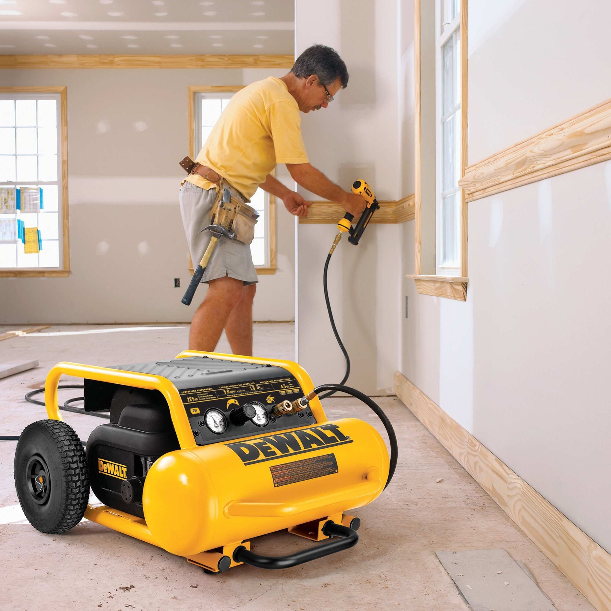 Worker nailing baseboard trim with the DeWalt 4.5 gallon compressor alongside