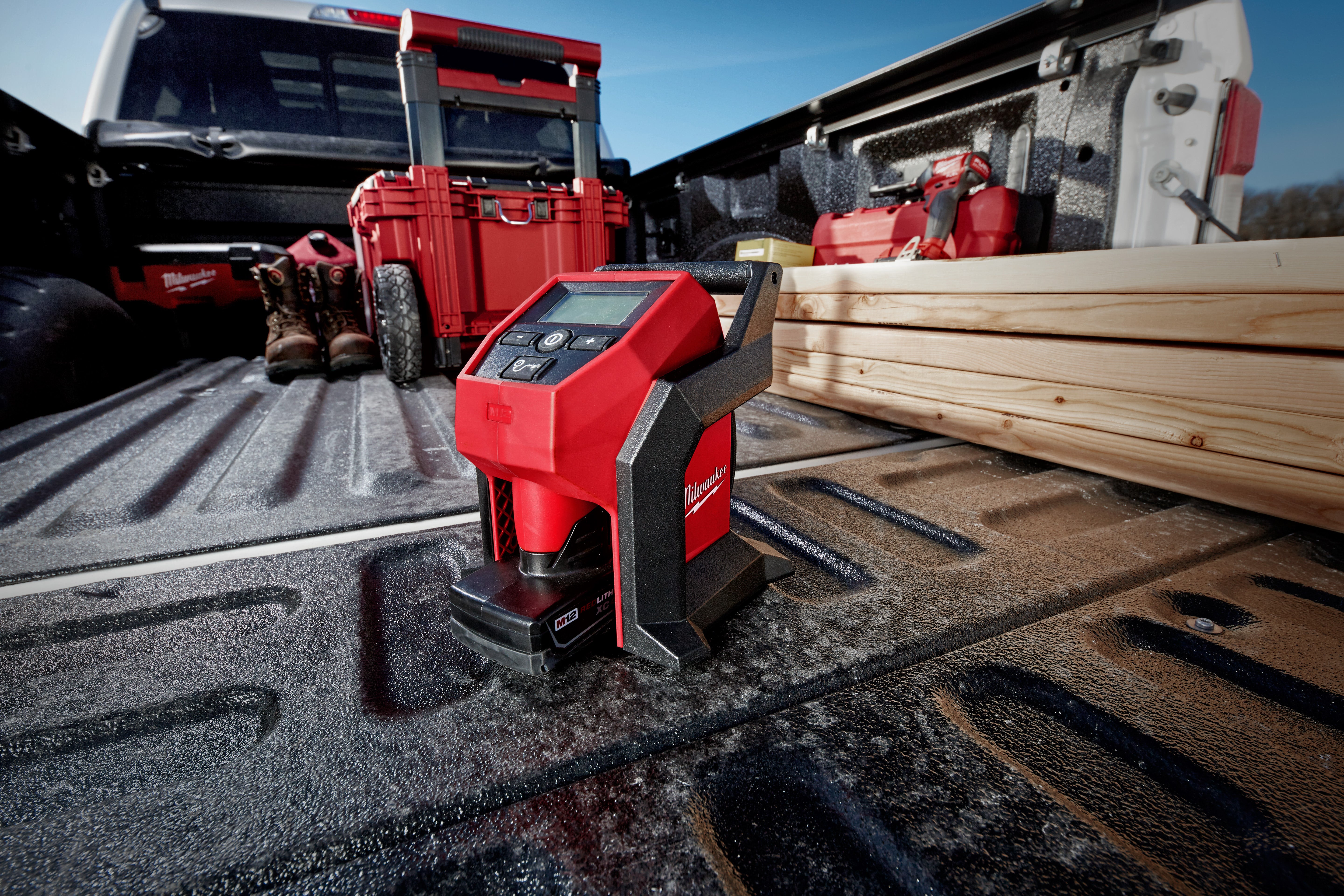 Milwaukee M12 compact inflator in a pickup bed beside PACKOUT boxes and tools