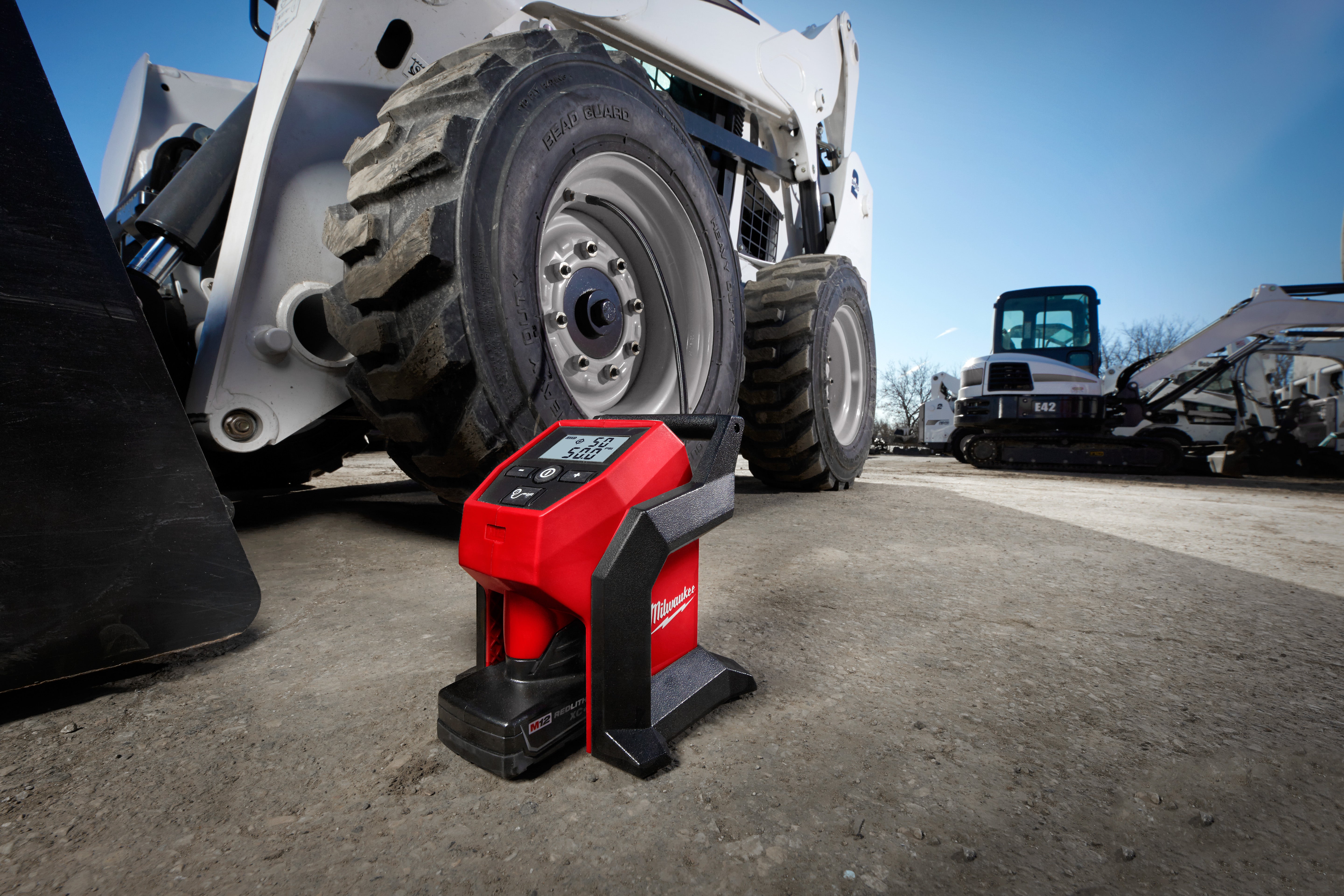 Milwaukee M12 compact inflator filling the tire of a skid-steer loader on a job site