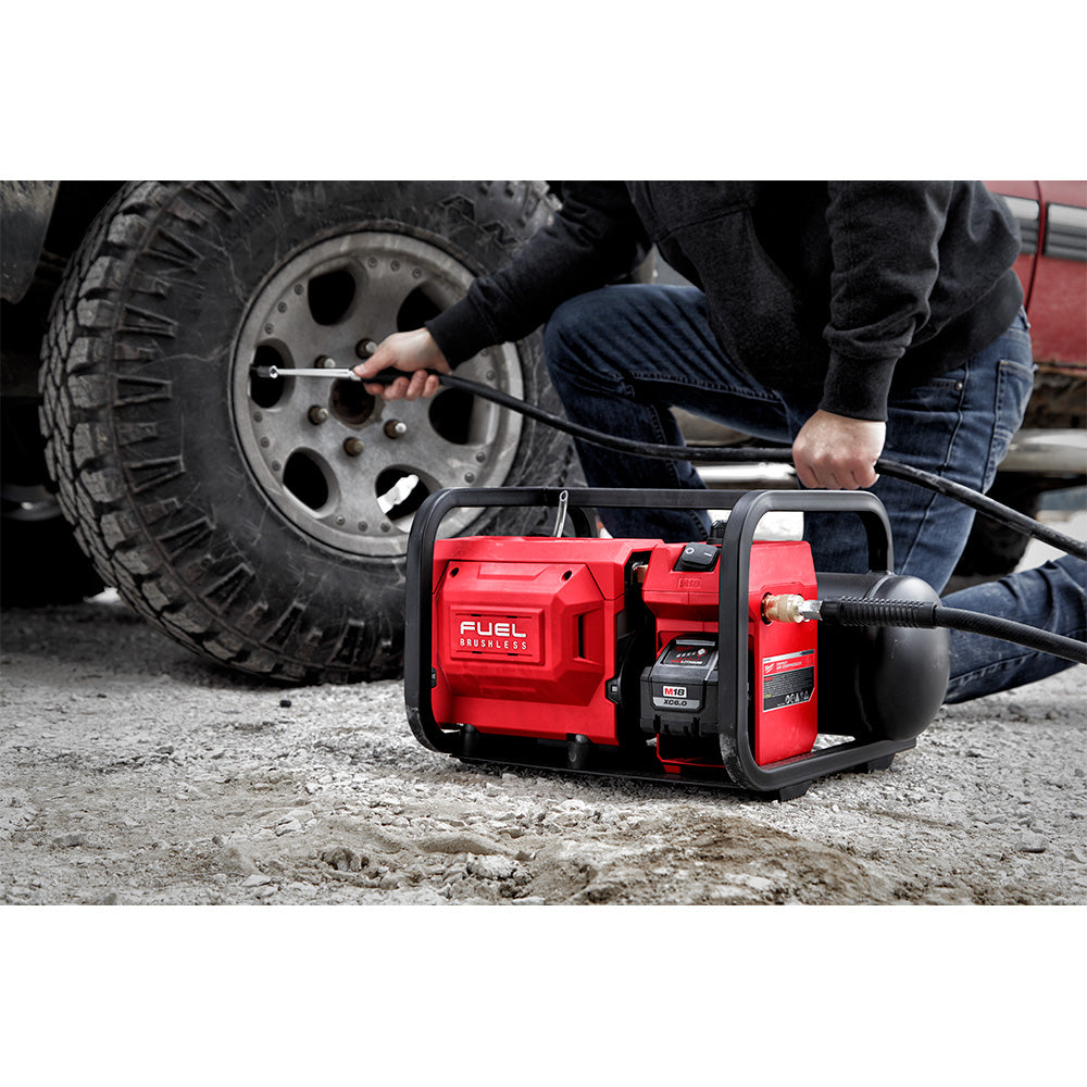 Worker using the M18 FUEL compressor to inflate a truck tire on a rough track