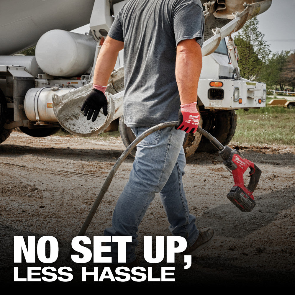 Worker carrying the M18 FUEL pencil vibrator past a mixer truck on a site
