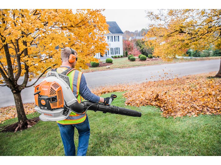 Landscaper in a high-visibility vest clearing fall leaves with a STIHL backpack leaf blower